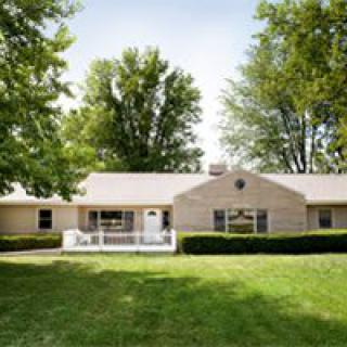 A suburban house with a large lawn and surrounding trees.