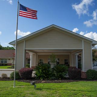A house with a front porch and an American flag flying on the lawn under a blue sky.