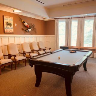 A cozy billiard room featuring a pool table, a row of chairs, and large windows allowing natural light.