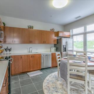 A spacious kitchen with wooden cabinets, modern appliances, and a dining area with a table and chairs, illuminated by natural light from large windows.