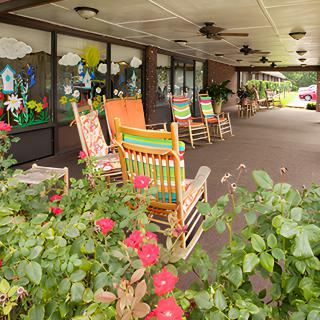 A porch with colorful rocking chairs and vibrant flowers.