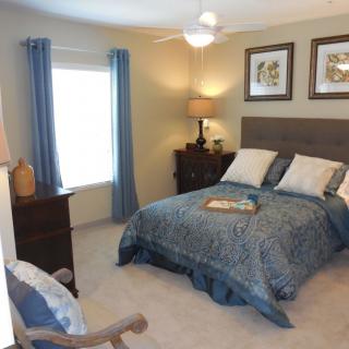 A cozy bedroom with a double bed, decorated with blue bedding and curtains, illuminated by table lamps.
