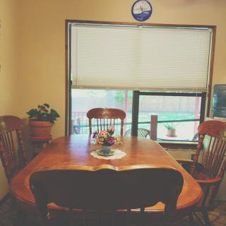 A cozy dining room with a wooden table and chairs, illuminated by natural light through a window with blinds.