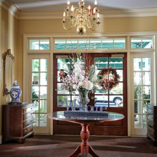 Elegant entrance with a chandelier, floral arrangement on a round table, and decorative mirrors and vases.