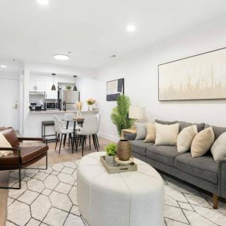 A modern living room with a stylish gray sofa, geometric coffee table, and elegant artwork, leading into a dining area.