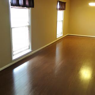 An empty room with hardwood flooring and two large windows.