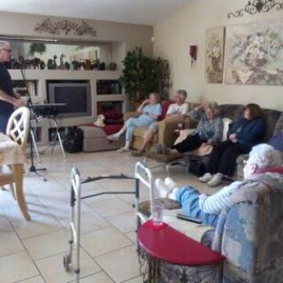 A group of people seated in a cozy living room, some with walkers nearby, watching TV.