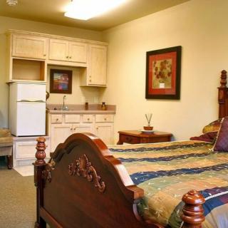 A cozy bedroom with a kitchenette featuring an ornate wooden bed and compact appliances.