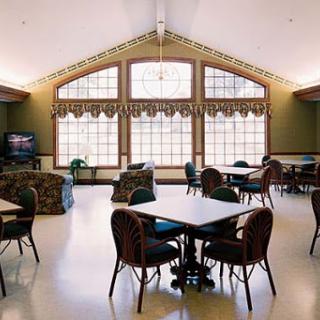 A bright and welcoming community dining area featuring round tables, chairs, and large windows that let in plenty of natural light.