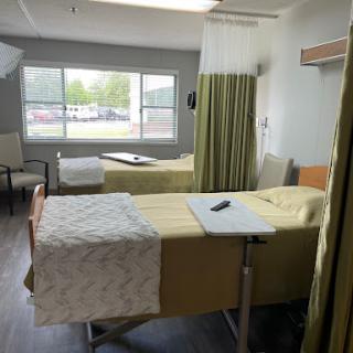 A clean and organized hospital patient room with two beds and a view out the window.