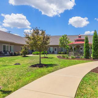 A scenic view of a landscaped garden with a pathway leading to a large building under a clear blue sky.