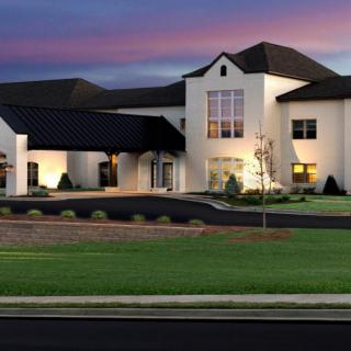A modern building with a landscaped lawn and driveway at dusk.