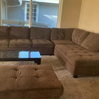 A cozy living room featuring a brown sectional sofa, coffee table, and ottoman with a large window in the background.