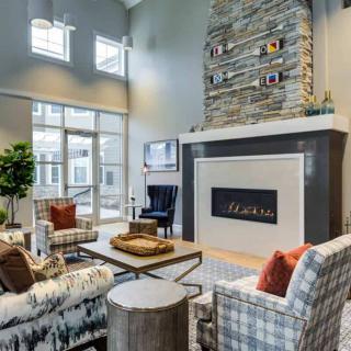 A modern living room with a high ceiling, featuring a stylish fireplace and large windows.