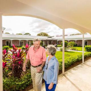 An elderly couple walking together in a garden area of a retirement community.