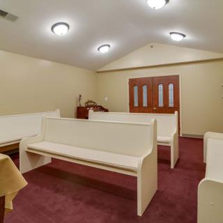 An interior view of a small church with white pews and carpeted flooring.