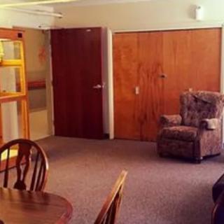 A cozy living room with a wooden table and chair set, a comfortable armchair, and wooden doors.