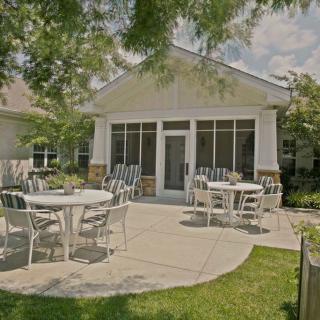 A sunny backyard patio with white outdoor furniture and a screened porch.