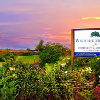 A picturesque landscape featuring a colorful sunset, vibrant flowers, and a welcoming sign.