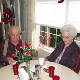 An elderly couple sitting at a table adorned with red Valentine's Day decorations and roses.
