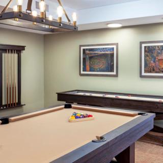 A stylish game room featuring a pool table and shuffleboard with elegant lighting and artwork on the walls.