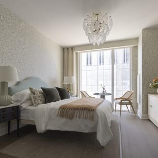 A contemporary bedroom with a chandelier, neutral color scheme, and modern furnishings.