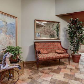 A cozy interior space featuring a patterned bench, a large mirror, potted plants, decorative artwork, and tiled flooring.