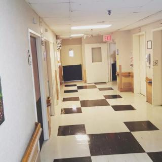A hospital corridor with checkered flooring and several doors along the walls.