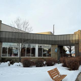 A snowy landscape featuring a modern building with large windows and an empty bench in the foreground.