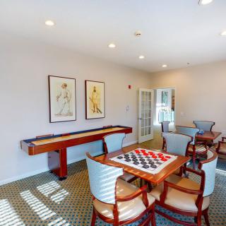 A well-lit game room featuring a shuffleboard table and a chessboard with chairs around it.