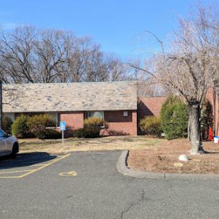 A view of a single-story building surrounded by a parking lot and barren trees in winter.