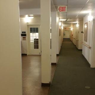 A well-lit interior hallway featuring doors, an exit sign, and green carpeting.