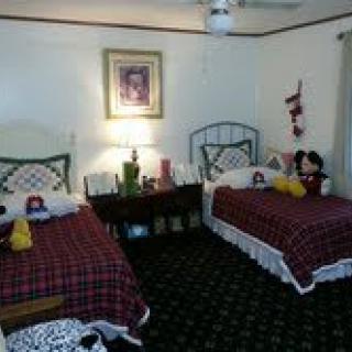A cozy bedroom with twin beds featuring plaid bedding and decorative pillows, well-lit by a bedside lamp and adorned with wall art.