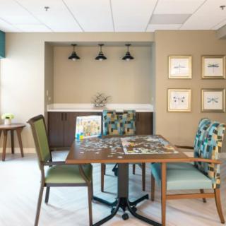 A cozy room featuring a table with a puzzle in progress, surrounded by chairs and adorned with artwork and stylish lighting.