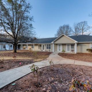A suburban ranch-style house with a walkway leading to the entrance and trees in the front yard.