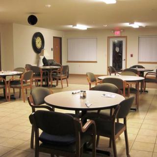 An empty dining area with round tables and chairs, softly lit by overhead lights.