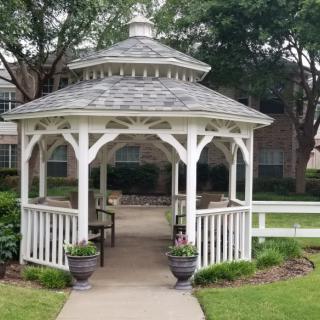 A white gazebo situated in a garden with potted plants and a pathway.