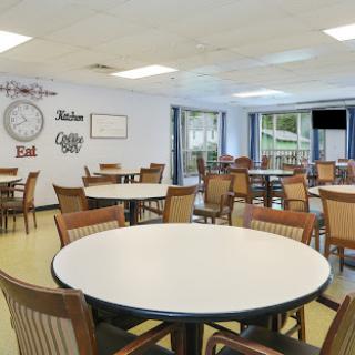 A spacious dining area featuring round tables and wooden chairs, illuminated by natural light.