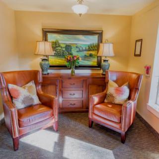 A cozy living room corner featuring two leather chairs, a wooden cabinet, and a painting with lamps on either side.