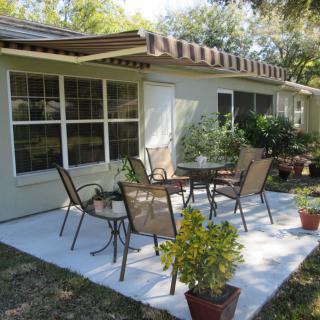 A cozy backyard patio with chairs and a table surrounded by potted plants.