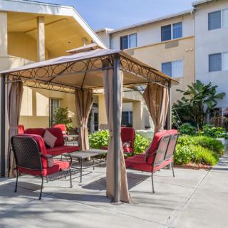 A cozy outdoor seating area with red-cushioned patio furniture under a gazebo in front of an apartment building.