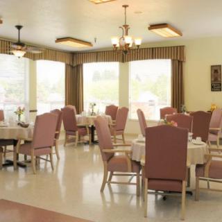 A well-lit dining room with neatly arranged tables and chairs, surrounded by large windows with curtains.