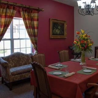 A cozy dining room with a table set for a meal, featuring a floral arrangement and elegant curtains.