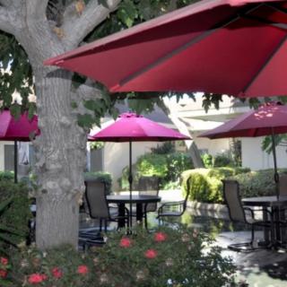 A peaceful outdoor patio with tables, chairs, and red umbrellas surrounded by a garden setting.