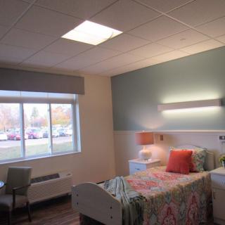 A well-lit hospital room with a bed, colorful bedding, and a large window.