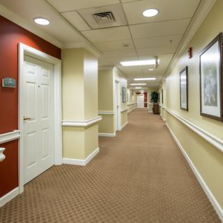 A well-lit hallway in a building, featuring carpeted flooring, doors on both sides, and framed artwork on the walls.