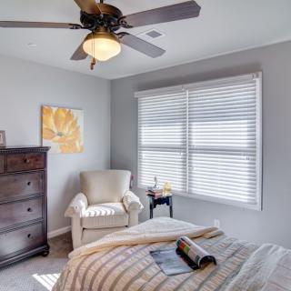A cozy bedroom with natural light, featuring a bed, armchair, dresser, and ceiling fan.