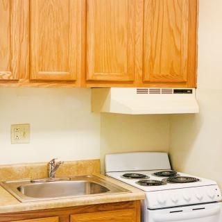 A compact kitchen with wooden cabinets, a stainless steel sink, and a stove with an overhead hood.