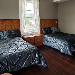 A cozy bedroom with two beds featuring dark bedding, separated by a window with white curtains.