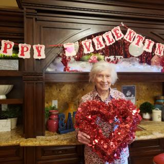 A cheerful elderly woman holding a heart-shaped decoration in celebration of Valentine's Day.